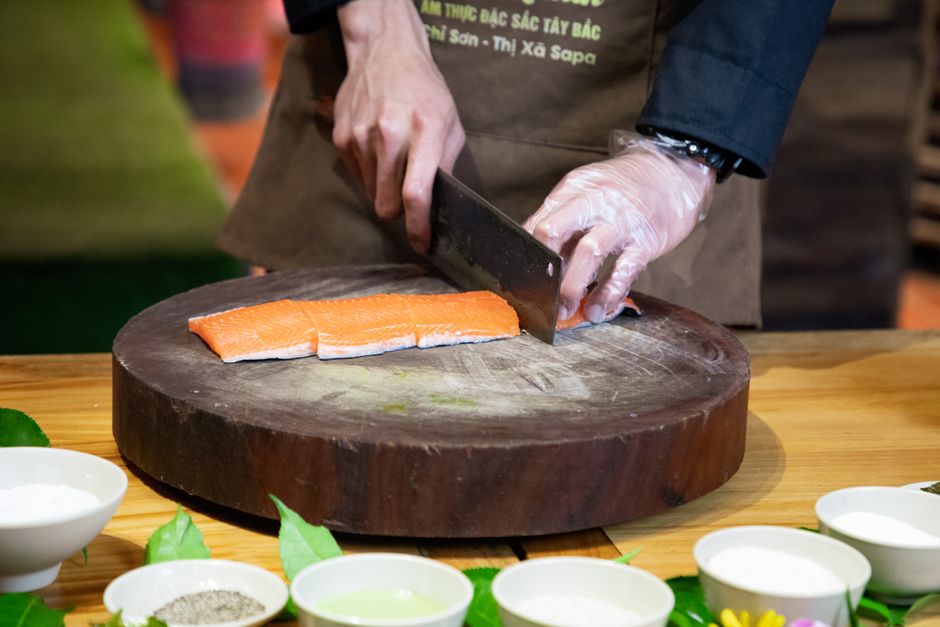 A chef skillfully cuts fresh salmon on a wooden board, surrounded by kitchen ingredients.