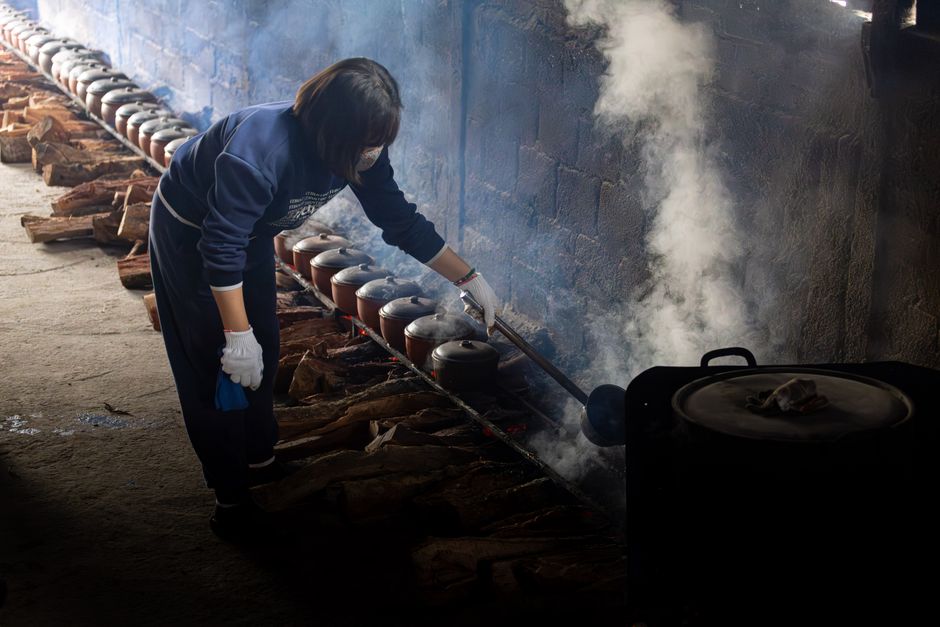A woman in Vietnam tends to clay pots cooking over an open fire, creating traditional cuisine.